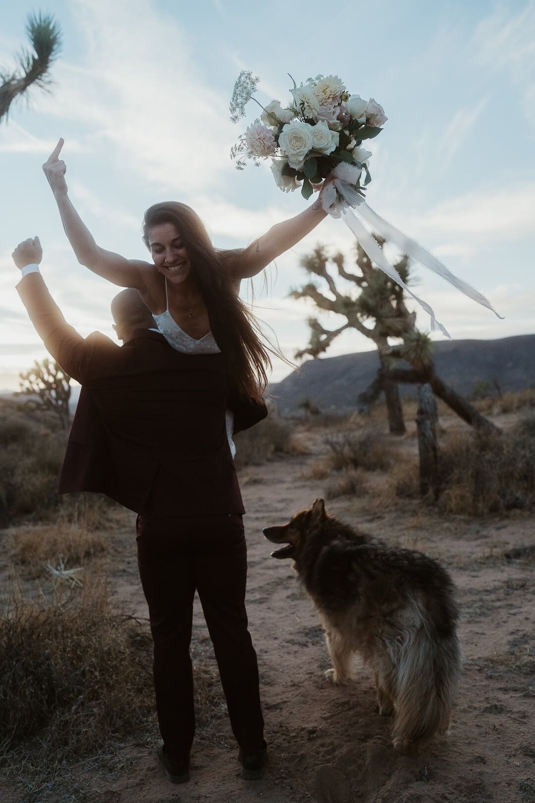 Joshua Tree Elopement. Groom carries the bride on his shoulder, there dog tags along.