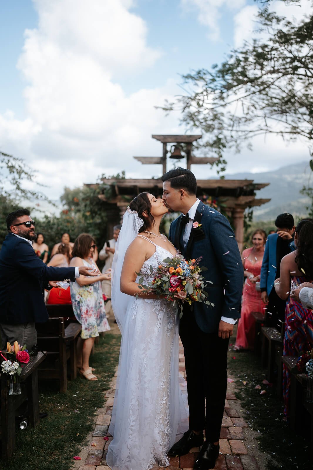 Wedding at Hacienda Siesta Alegre. Couple in wedding attire kiss as flowers fall around them.