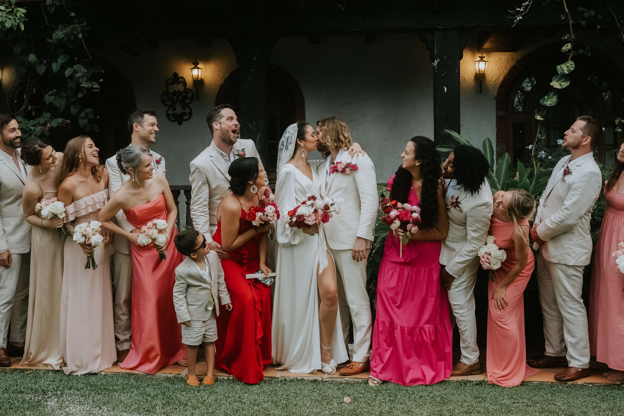 Wedding party at Hacienda Siesta Alegre. Bride and groom kiss while the wedding party cheers.