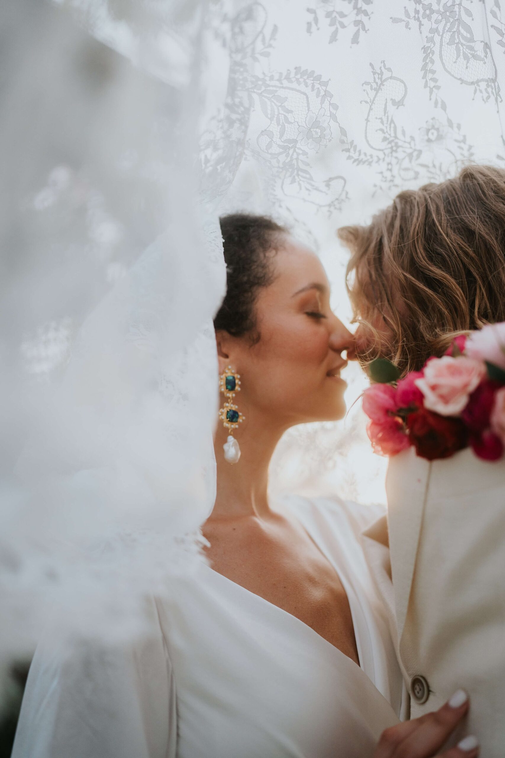 Couple in wedding attire, kiss under the veil.