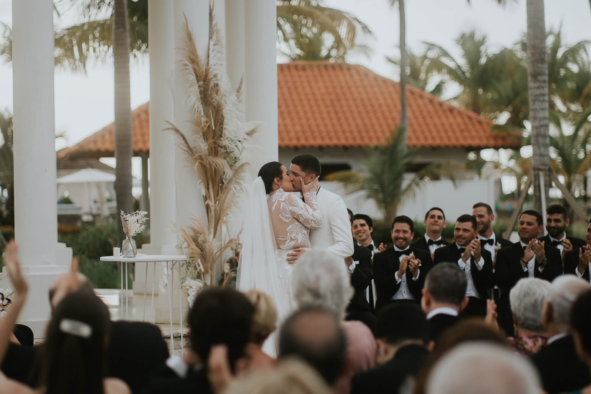 Wedding at St Regis Puerto Rico. Couple in wedding attire share their first kiss as husband and wife, the crowd cheers them on.